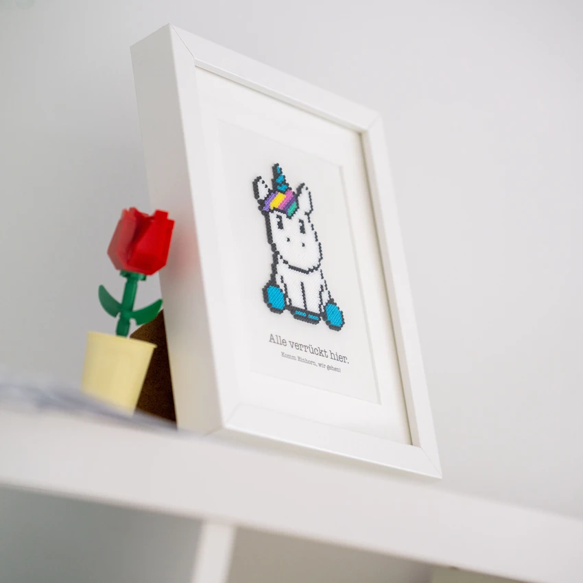 Gerahmtes Einhornbild und LEGO-Blume auf Regal.