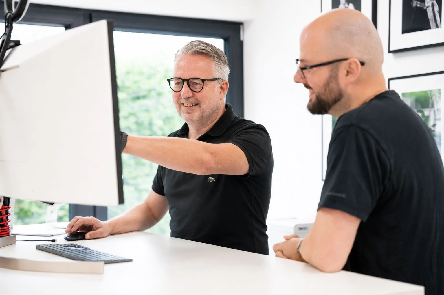 Zwei Männer im Gespräch an einem Schreibtisch mit Computer.