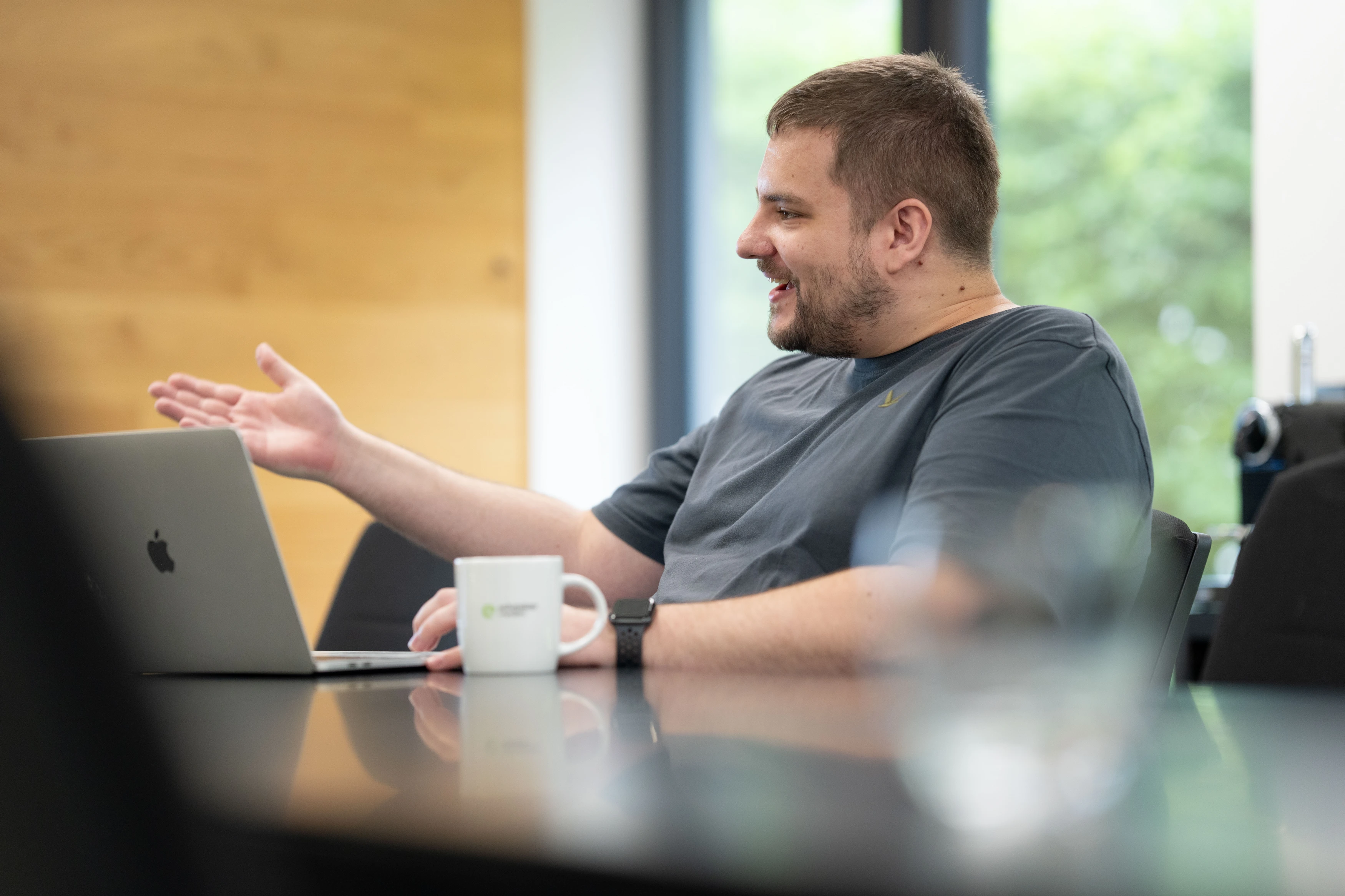 Mann spricht an einem Tisch mit Laptop.