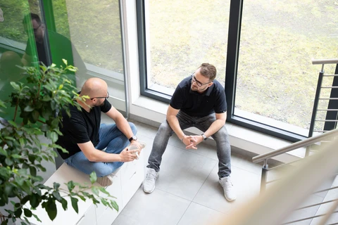 Zwei Männer sprechen an einem Fenster im Büro.