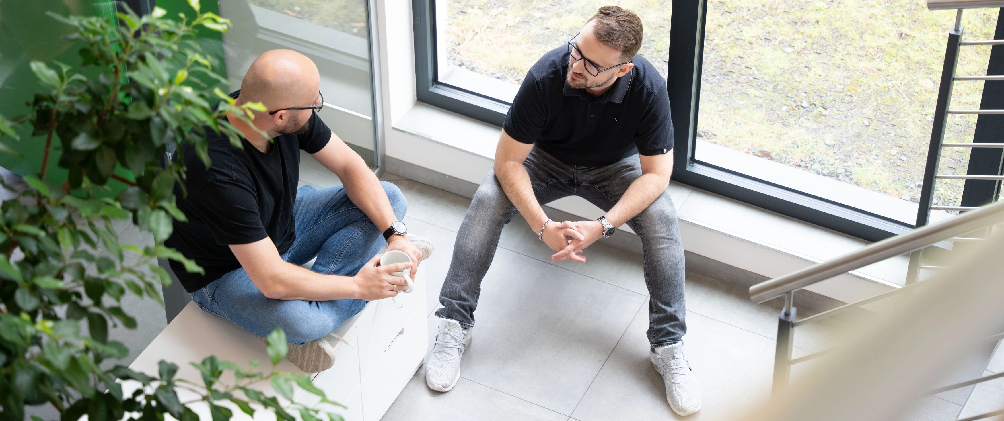 Zwei Männer sprechen an einem Fenster im Büro.