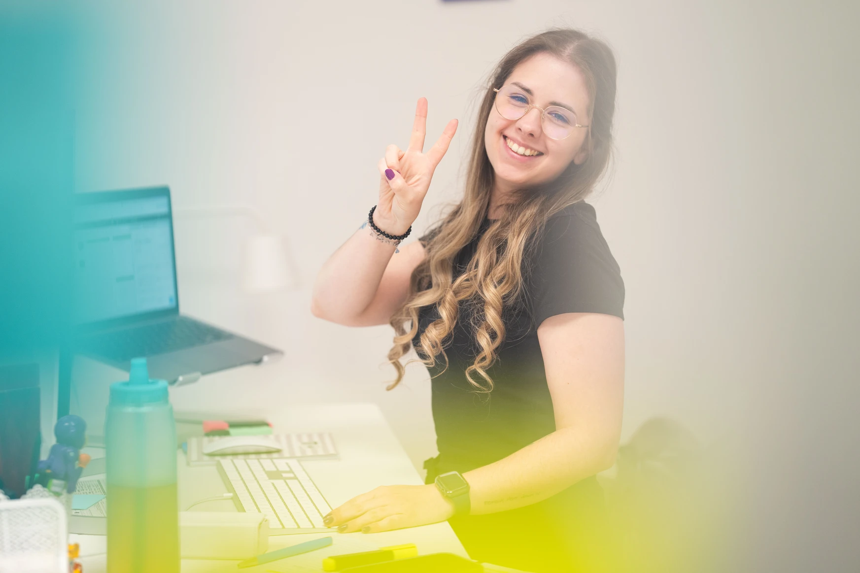 Frau lächelt und zeigt Peace-Zeichen am Schreibtisch.